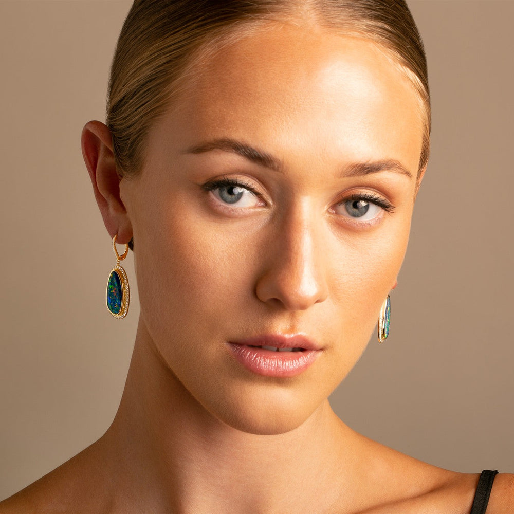 Model wearing one-of-a-kind 18k yellow gold Australian boulder opal and diamond halo earrings with vivid blue-green color play