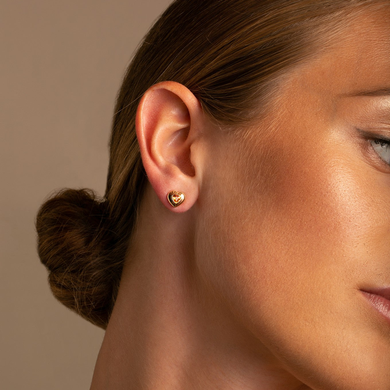 Crafted in luminous 14k yellow gold, these stud earrings showcase the vibrant hues of Spessartite Garnet in a classic heart cut, shown on model