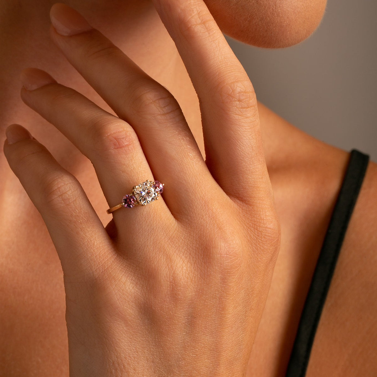 Three Stone Cushion Cut Moissanite and Natural Pink Sapphire ring set in a high polish 14k yellow gold setting on model