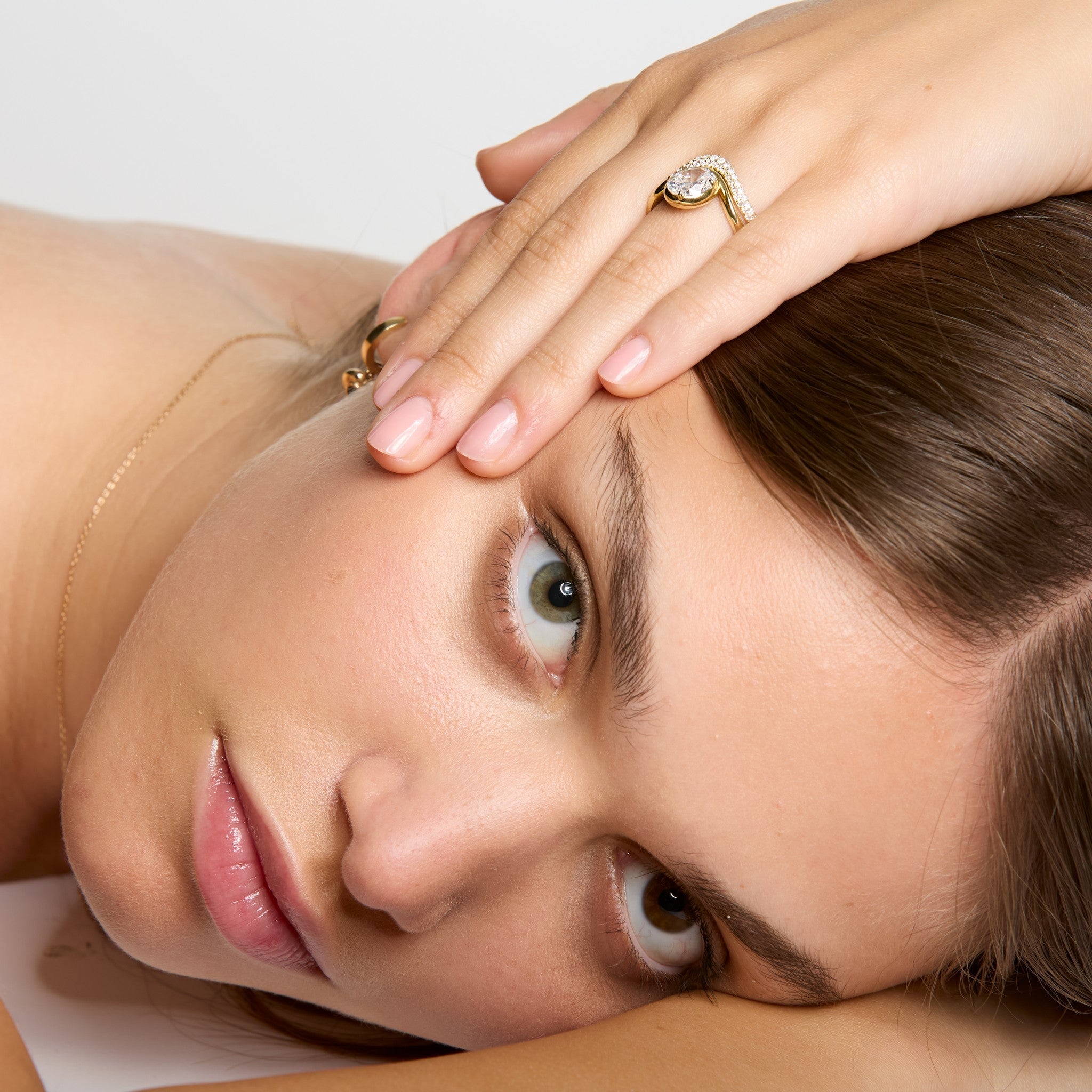 Thomas Laine Wave Collection oval diamond solitaire — fluid curves, modern bezel–claw hybrid, shown on model with handmade diamond pave band